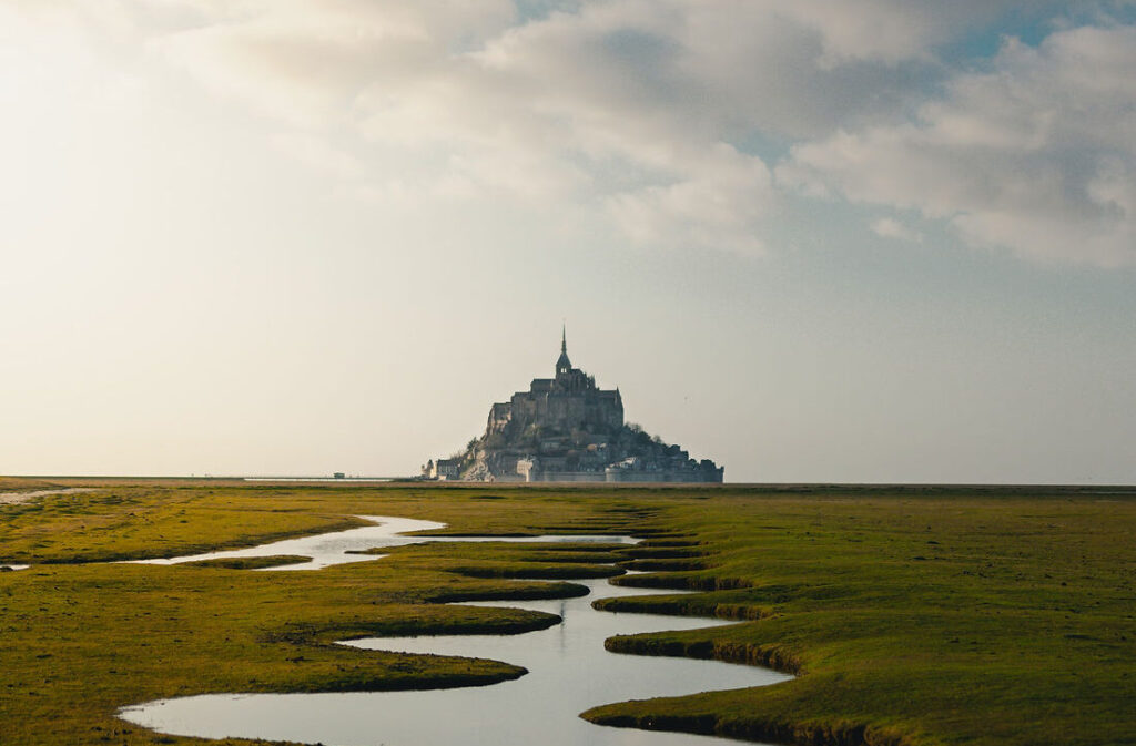 Mont Saint-Michel in the distance with a winding river surrounded by lush green grass