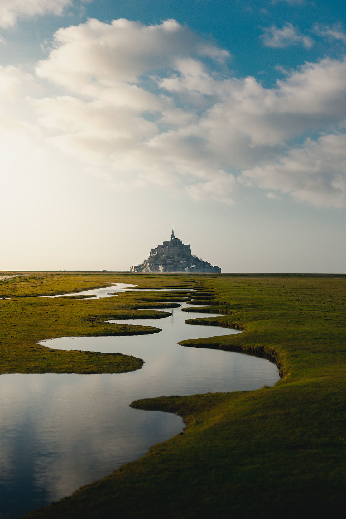 Mont Saint-Michel in the distance with a winding river surrounded by lush green grass
