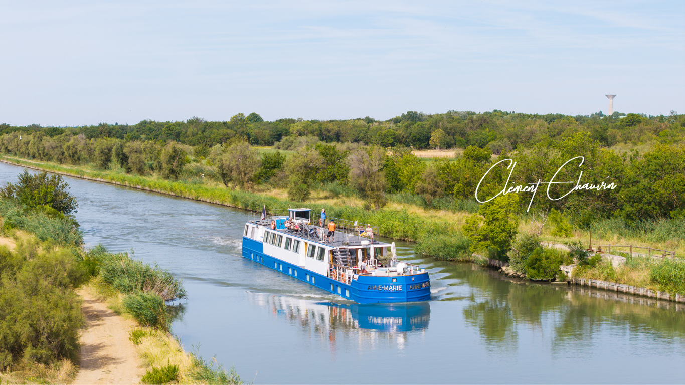 MS Anne-Marie canal barge cruising along the Canal du Rhône near Sète under blue skies, surrounded by peaceful waterways and lush landscapes.